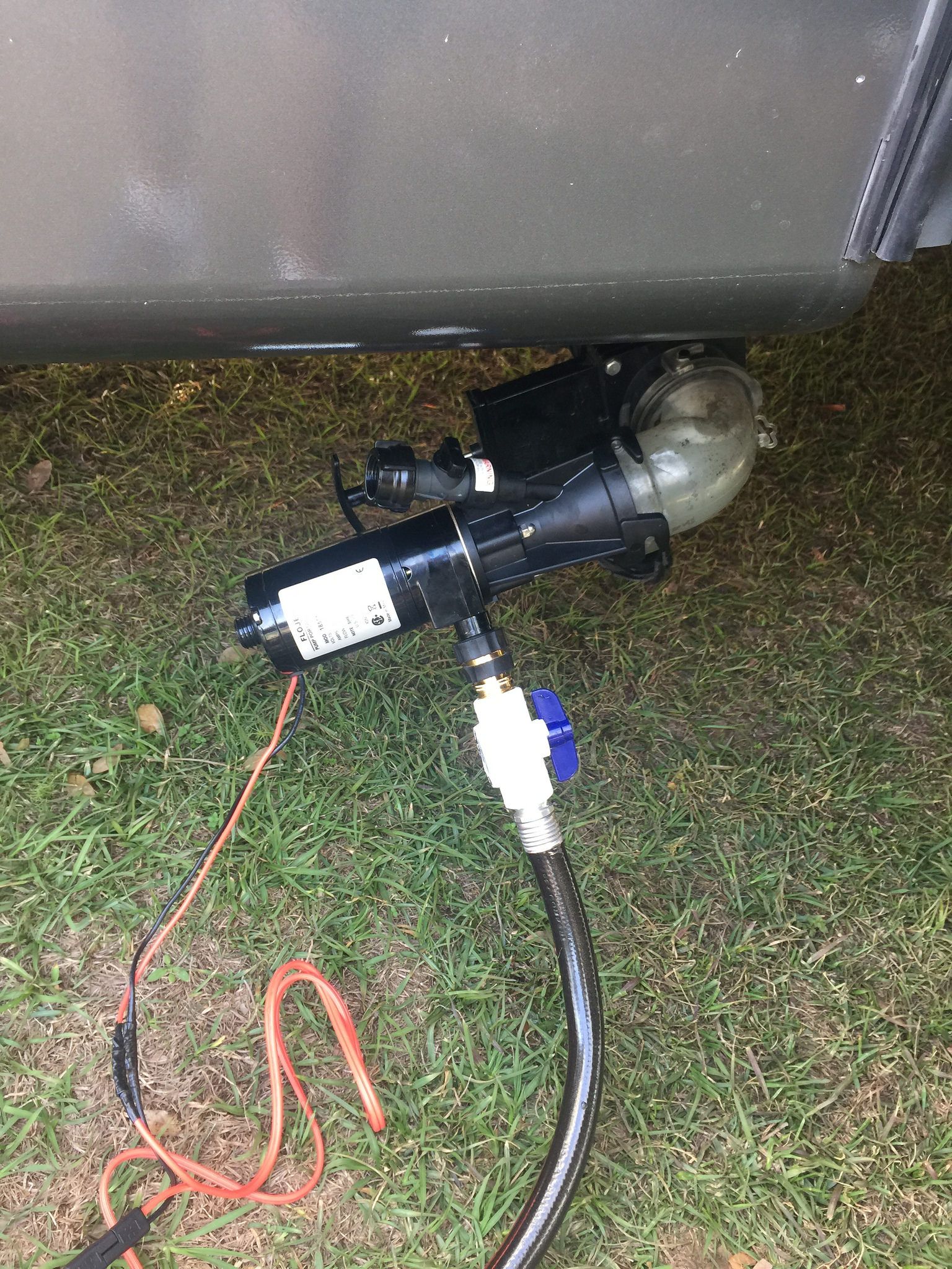 Black RV waste pump connected to a hose on grass. Orange and black wires are attached to the pump.