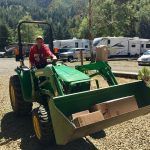 A man is driving a green tractor with a large bucket.