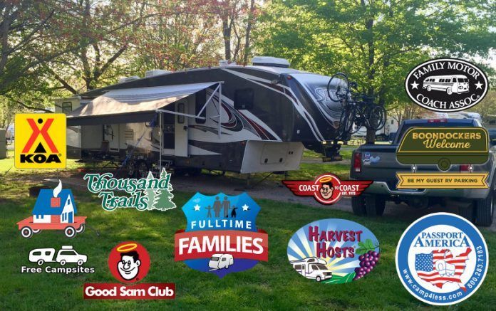 RV with logos for camping clubs on a grassy campsite.