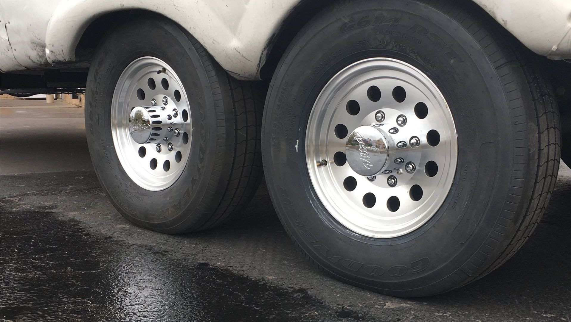 Two trailer tires with silver rims on wet asphalt.
