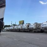 Row of white RVs parked outside under a blue sky, possibly a dealership.