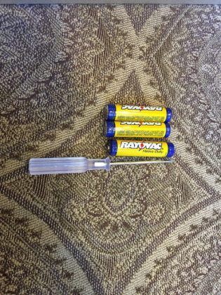 Three batteries and a screwdriver are sitting on a rug.
