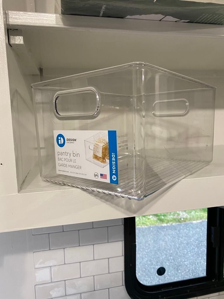 Clear plastic storage bin on a shelf in front of a window and tiled wall.
