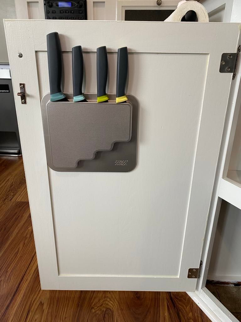 A white cabinet door with a magnetic knife block holding four knives; wood floor in the background.