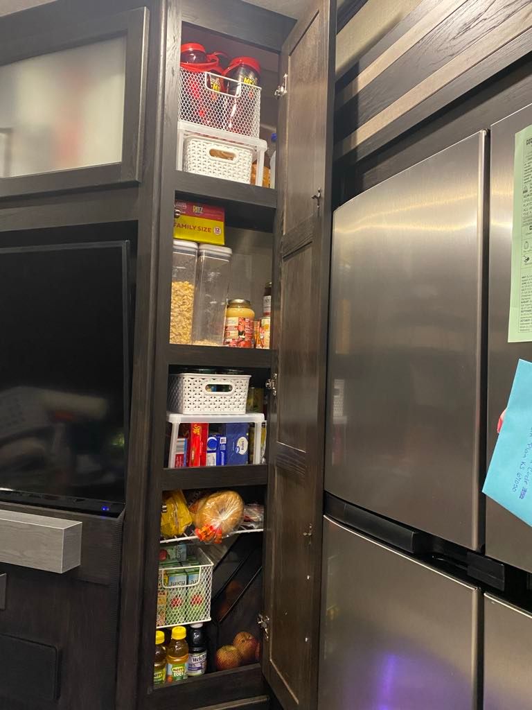 Pantry with food items, next to refrigerator, and entertainment center.