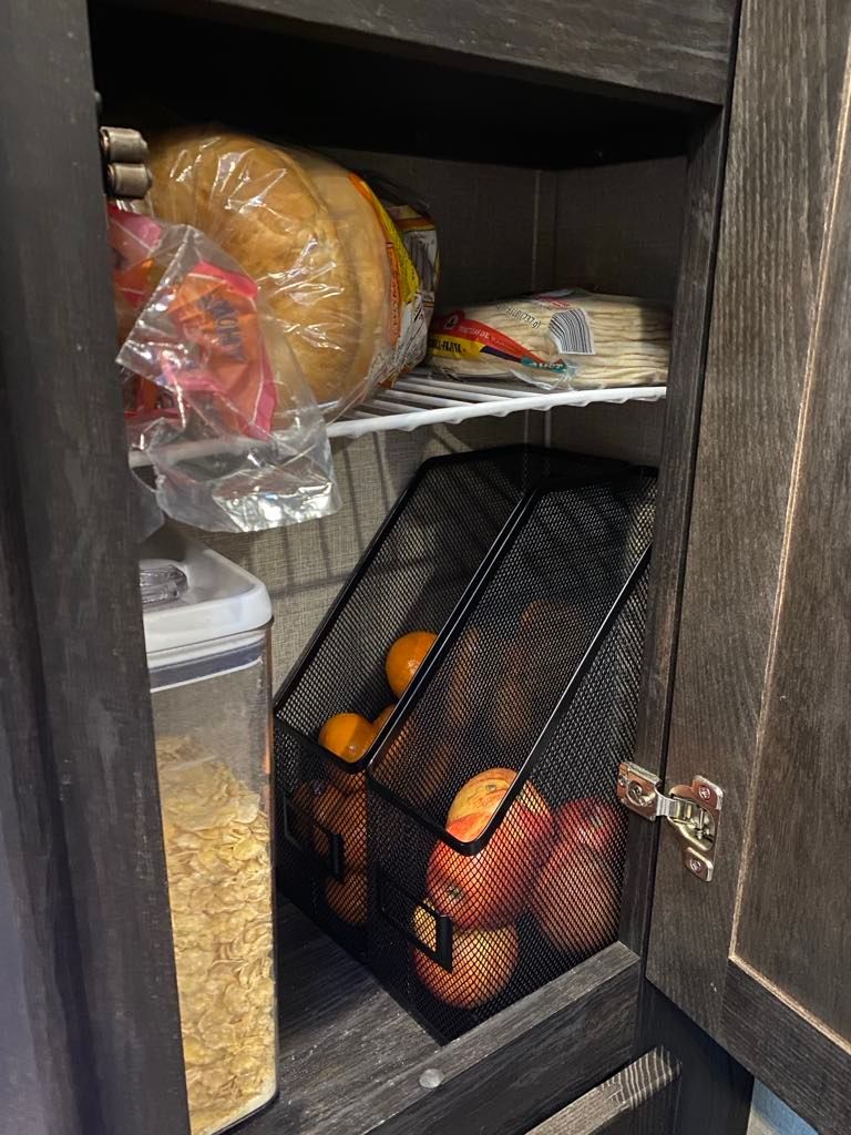 Pantry with bread, tortillas, cereal, and oranges in a wire basket. Dark wood cabinet.
