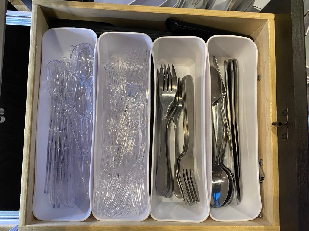 A drawer with four white rectangular compartments holding silverware and chopsticks.
