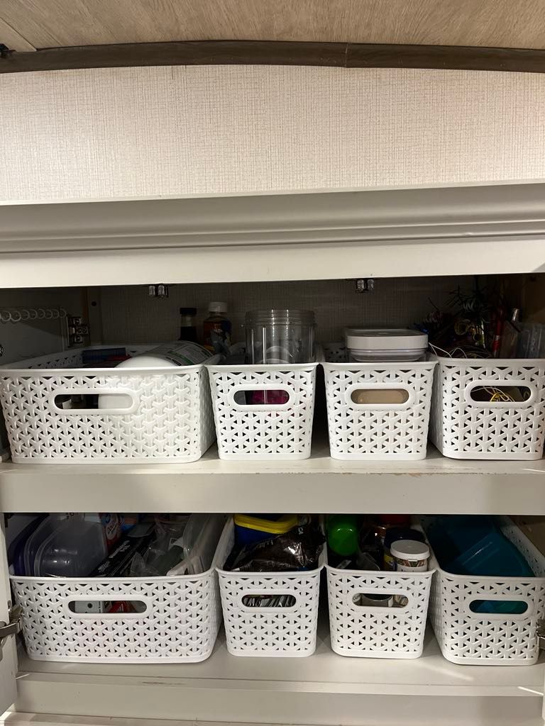 White pantry cabinet with organized baskets on shelves, filled with kitchen items.