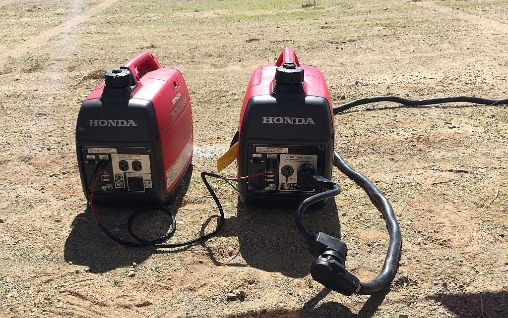 Two red portable generators on dry ground, cords connected.