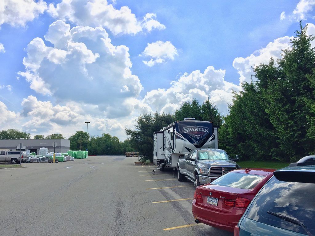 RV and pickup truck parked in a lot on a sunny day with puffy clouds.