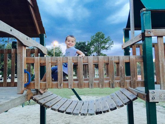A little girl is sitting on a wooden bridge at a playground