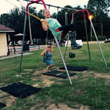 A girl is swinging on a swing set while another girl watches.