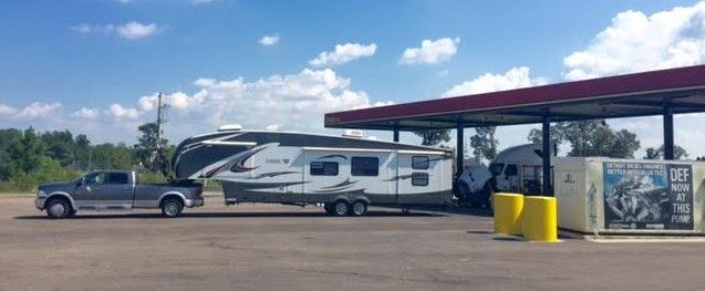 A truck is towing a trailer at a gas station.