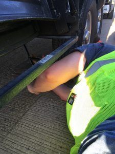 A person in a yellow vest is kneeling down next to a car.
