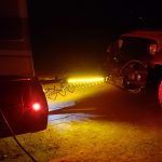 A car is being towed by a trailer at night.