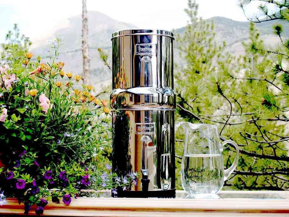 Stainless steel water filter with a pitcher of water on a deck, overlooking a mountain and greenery.