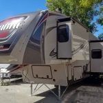 A rv is parked in a parking lot next to a tree.
