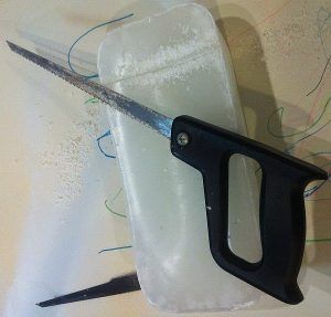 A saw is sitting on top of a piece of ice.