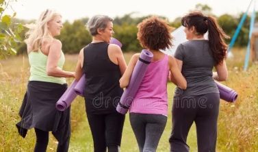 Four women walking outdoors in a field, carrying yoga mats at sunset.
