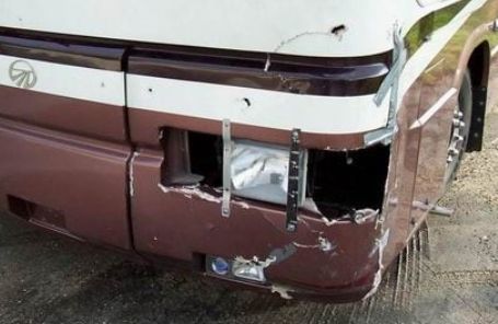 Damaged maroon motorhome front bumper with broken headlight and scraped white trim