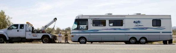 Tow truck towing a white RV trailer on a road