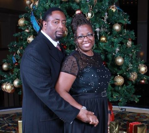 Couple posing in front of a decorated Christmas tree, dressed in black formal attire and smiling