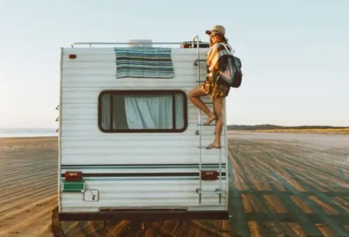 Person climbing a ladder on the back of a white RV in a flat desert landscape