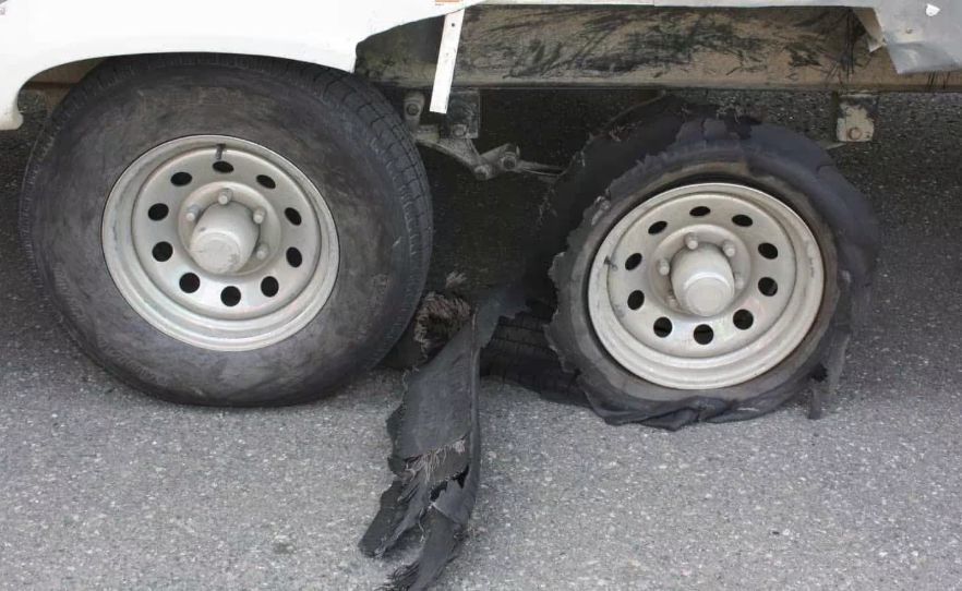 Two vehicle wheels on the same side, with the rear tire blown out and the front tire intact.