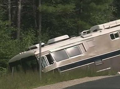 Overturned silver RV in a roadside ditch beside a forested road