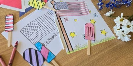Colorful paper crafts and drawings of popsicles and a sun on a wooden table