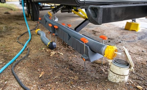 Grey hose with orange connectors on a trailer frame, outdoors on dirt ground.