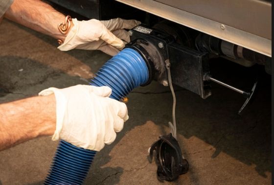 Gloved hands connecting a blue corrugated hose to a vehicle exhaust pipe under a car