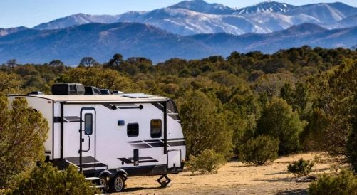White camper trailer parked in a wooded campsite with mountains in the background