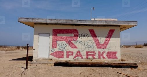 Small desert building with faded red “RV PARK” graffiti on the front wall.