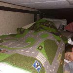 A person is laying under a bunk bed with a rug on it.