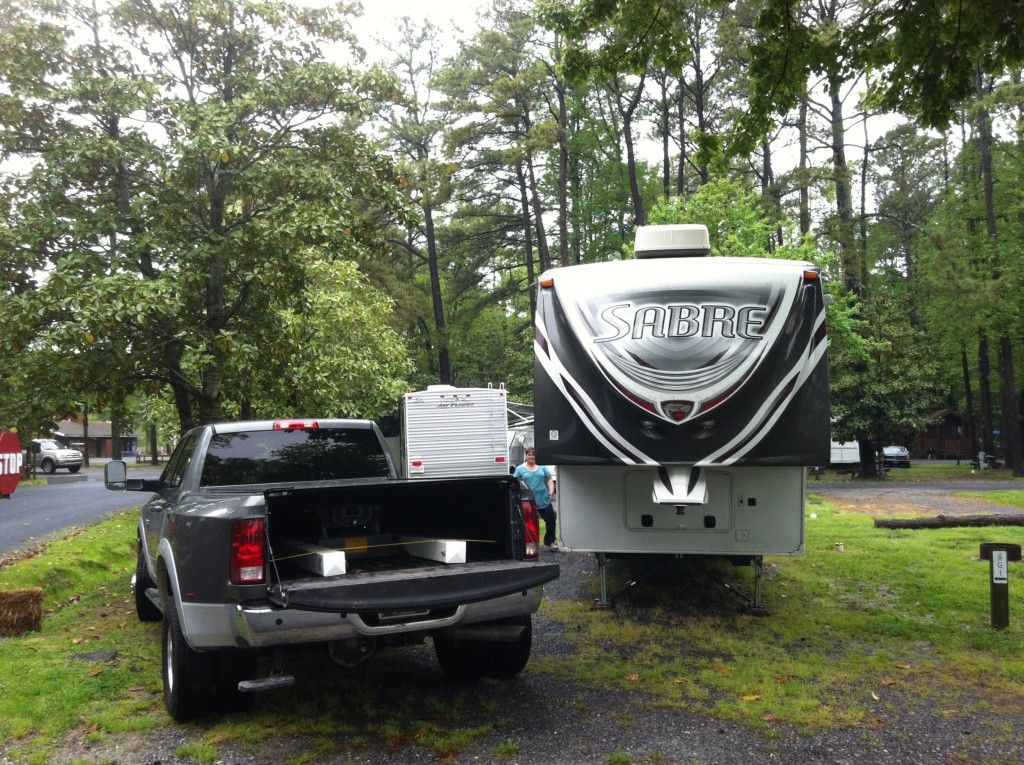 Gray pickup truck towing a large fifth wheel RV in a campground. Overcast day, trees in background.