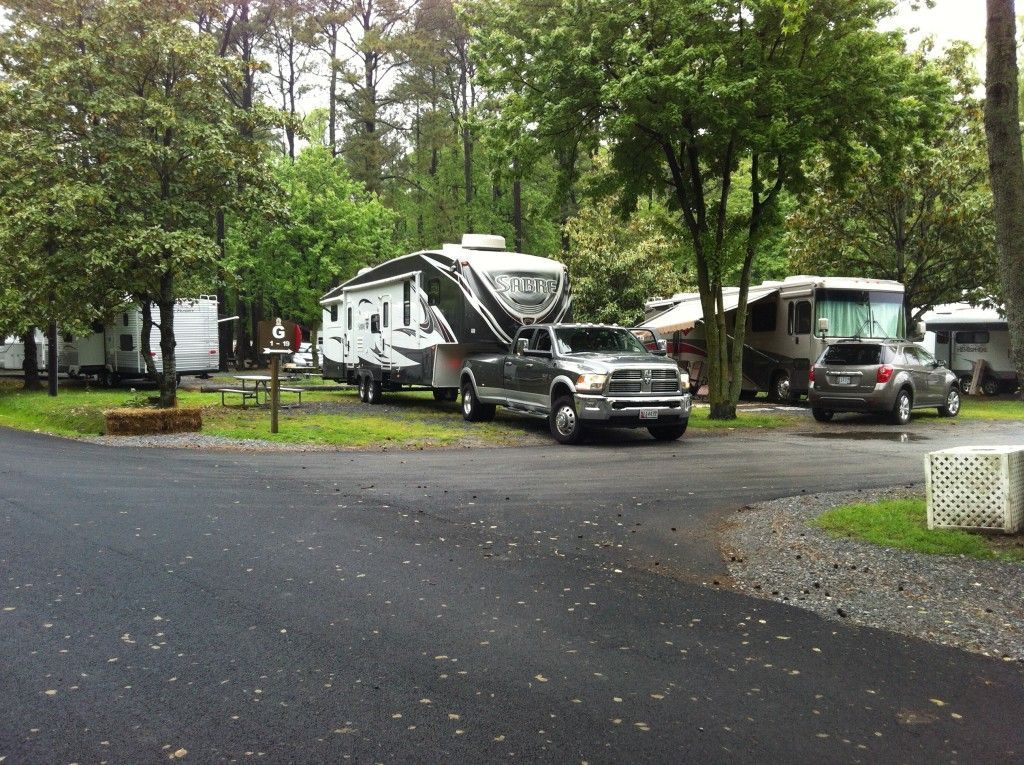 A truck towing a large camper in a campground with trees and other RVs.