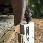 A lamp is sitting on top of a white pole next to a car.