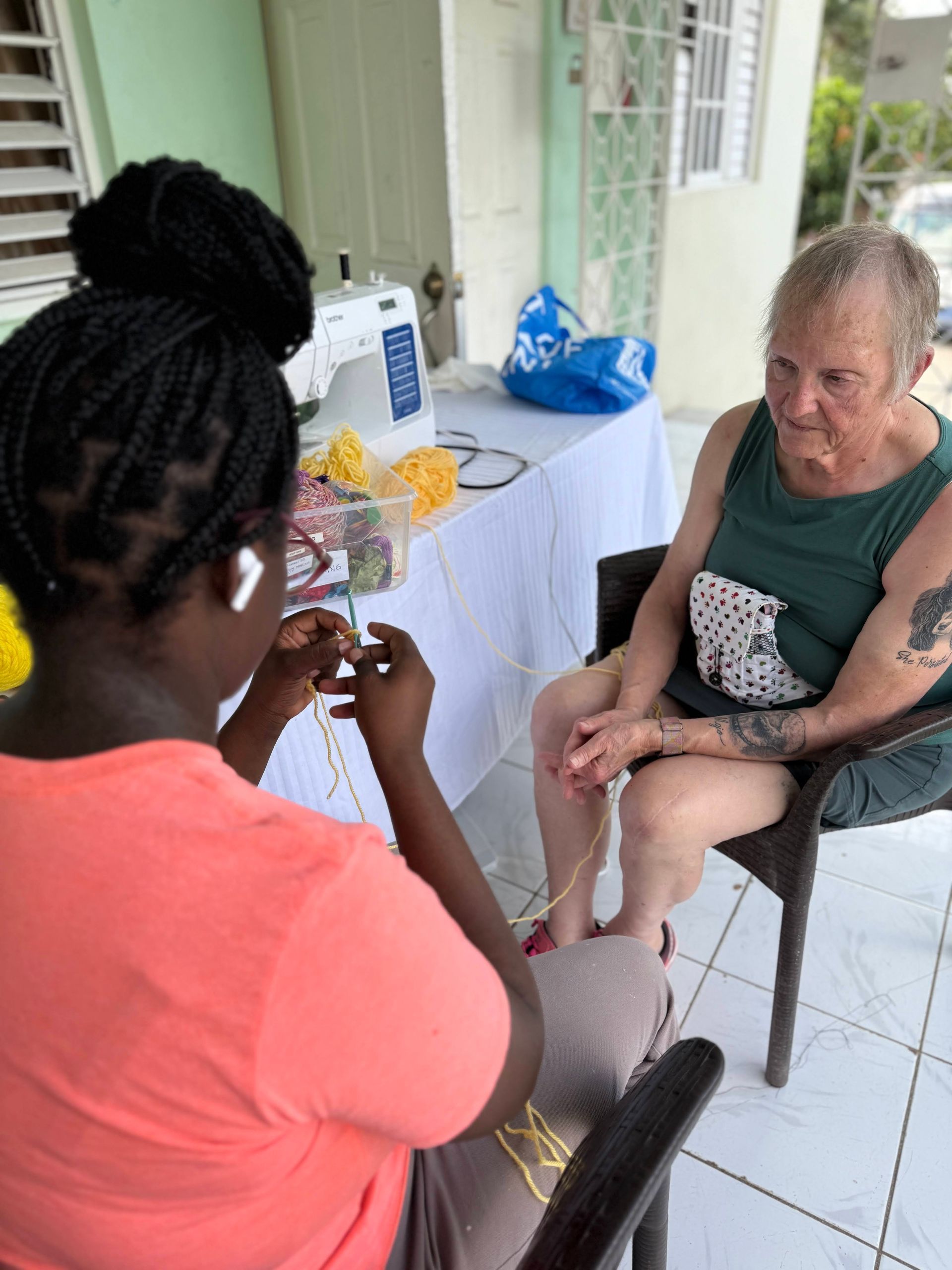 A woman is knitting while another woman sits in a chair.
