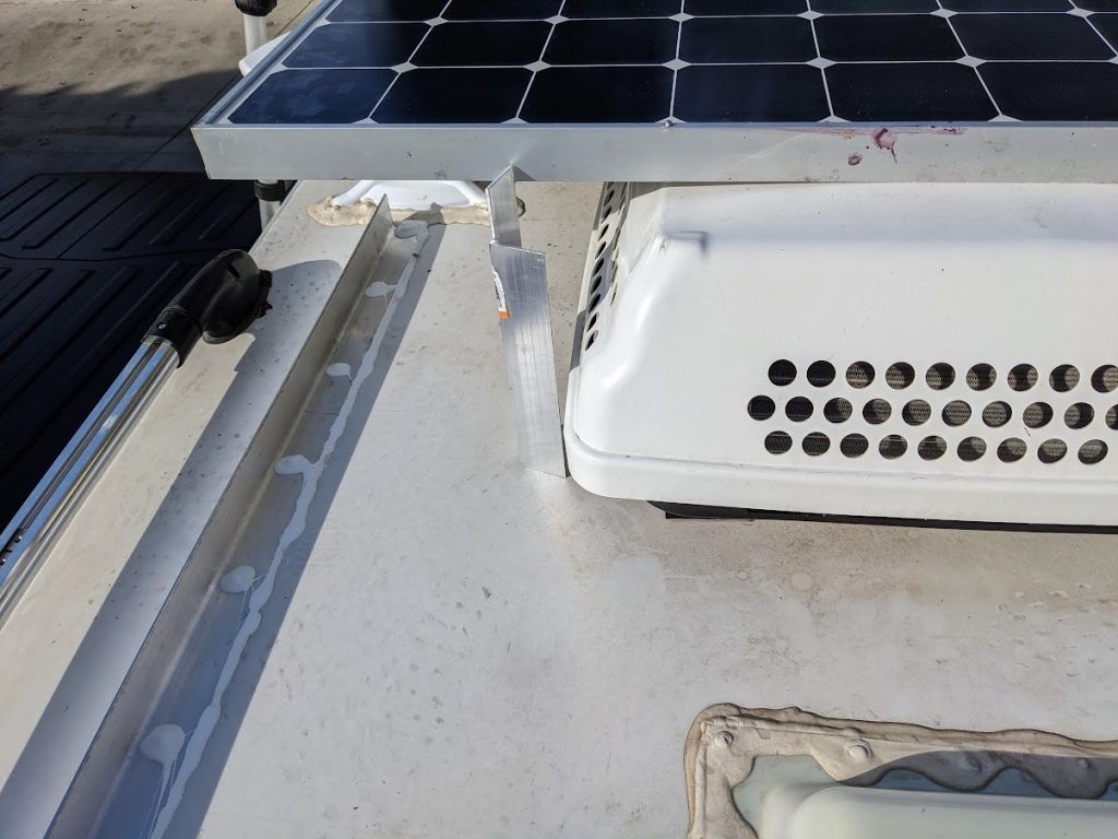 Solar panel mounted above a RV air conditioner on a white RV roof.