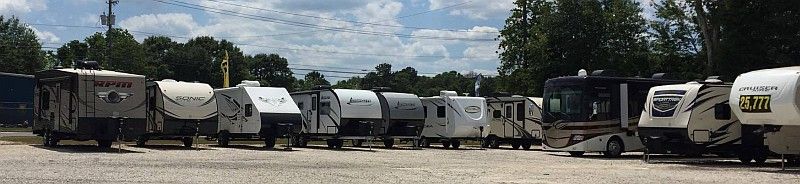 RVs parked in a lot, cloudy sky in the background, trees along the back.