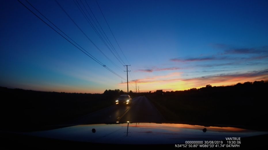 A car is driving down a road at sunset.