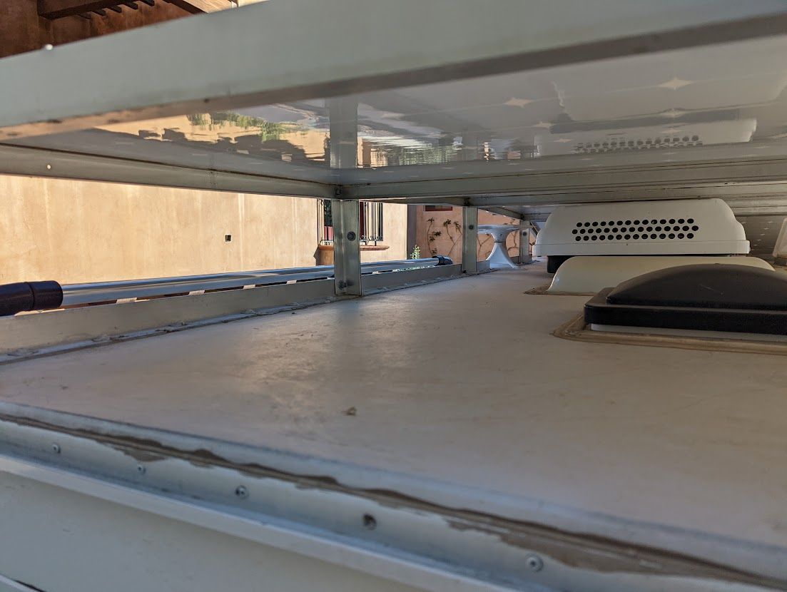 White RV roof with attached awning supports, vents, and skylight against a sunlit backdrop.