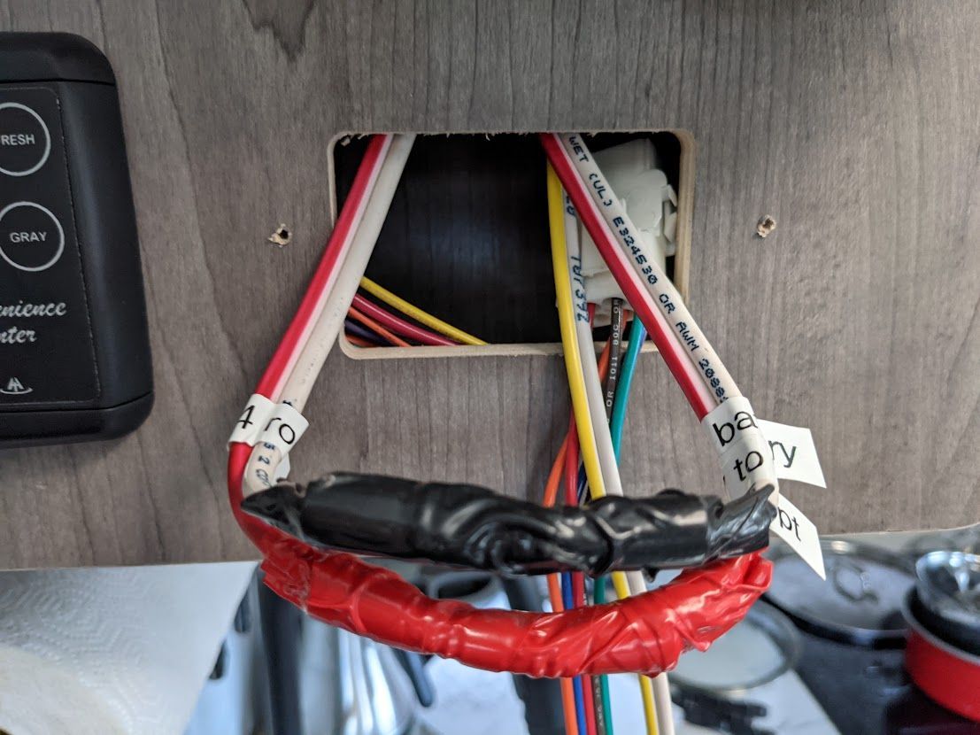 Close-up of exposed wires in a wooden panel with a control panel on the left. Wires are taped and bundled.