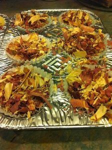 Aluminum foil tray filled with cupcakes covered in cheese and bacon.