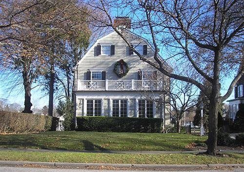 Dutch Colonial house with arched roof, white facade, balcony, and trees.