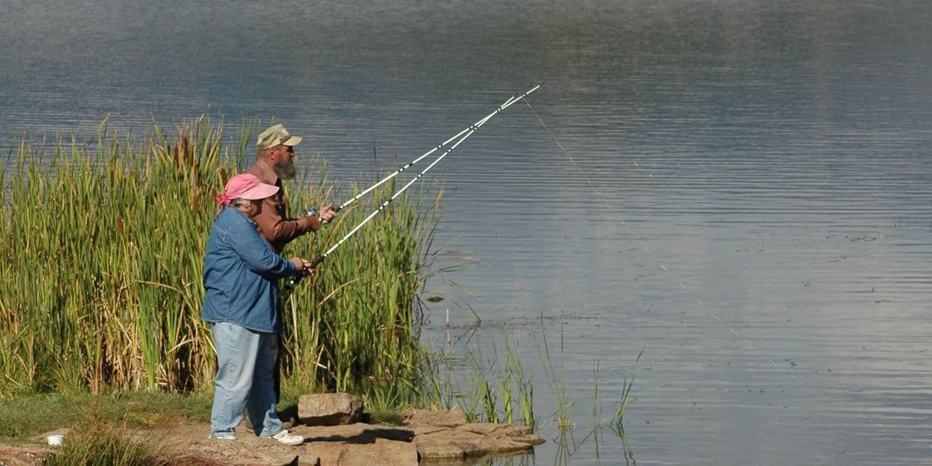 Two men are fishing in a lake with fishing rods.