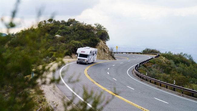 RV driving around a curved mountain road with ocean views.