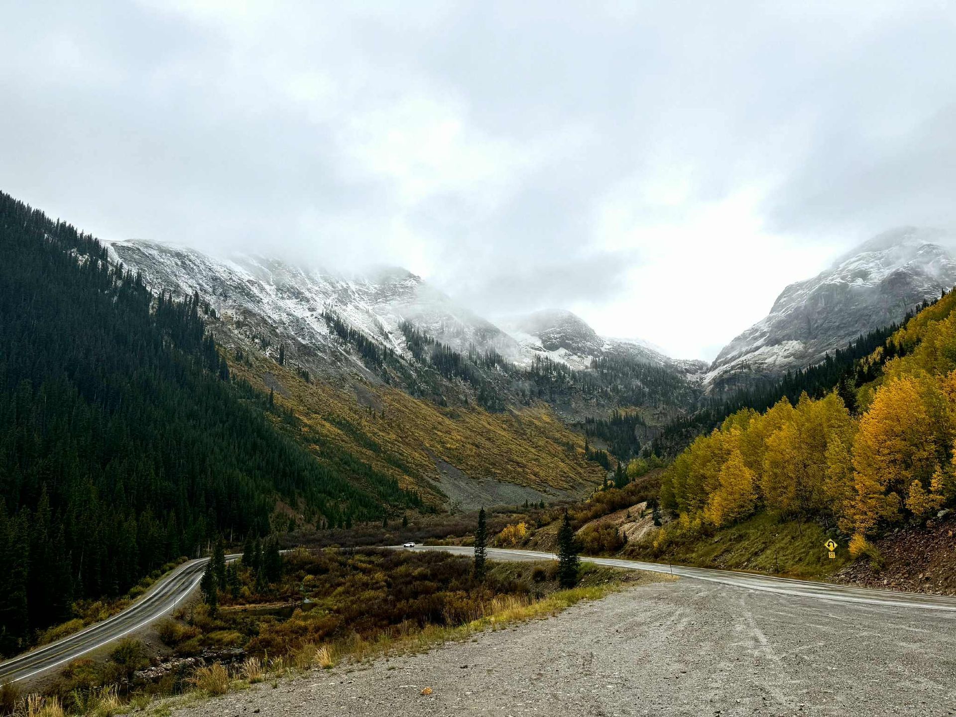 A road going through a mountain valley with snow on the mountains.