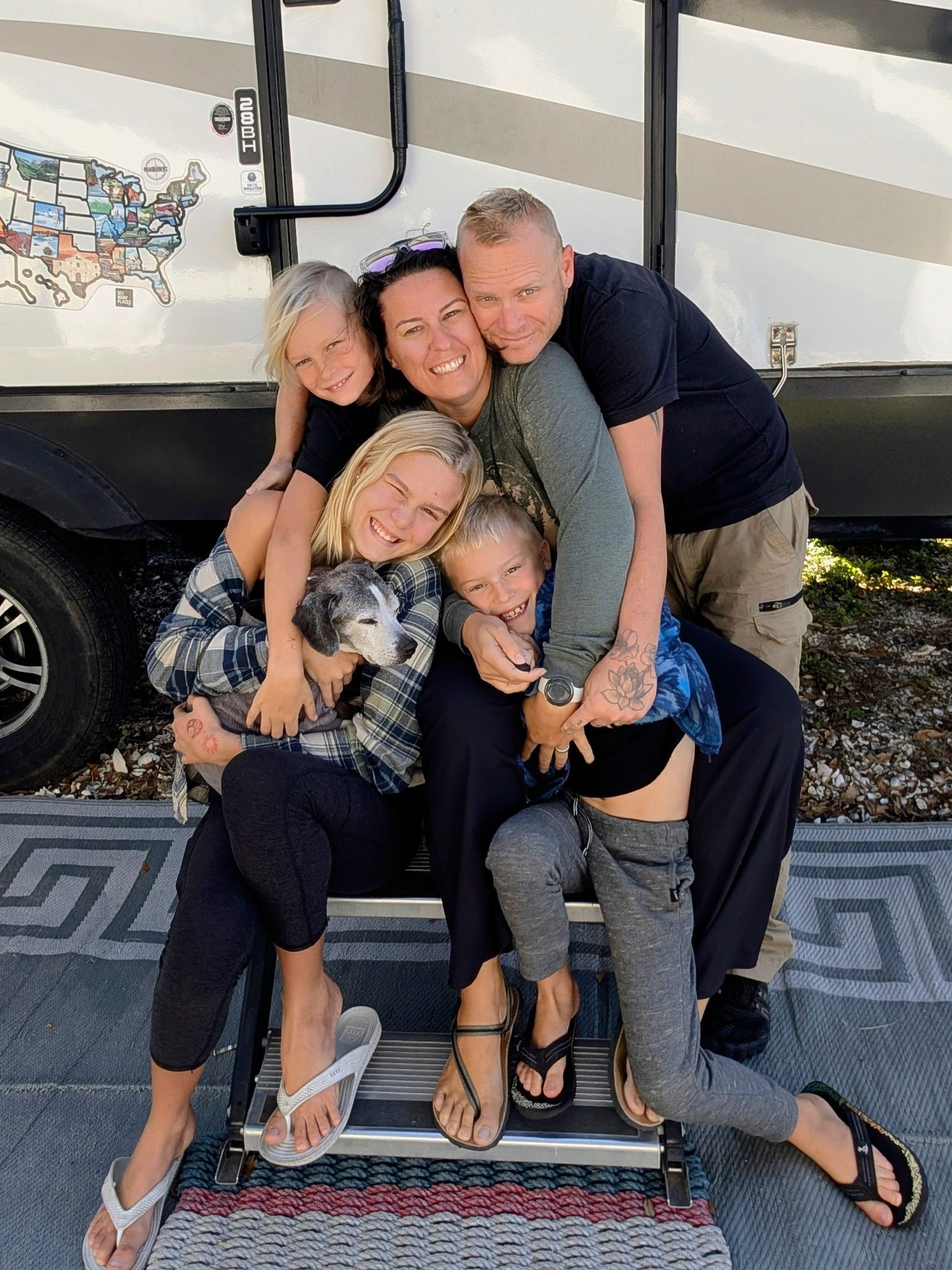 Family of five, embracing in front of RV. Two children hugging mother, another child and father in the group.